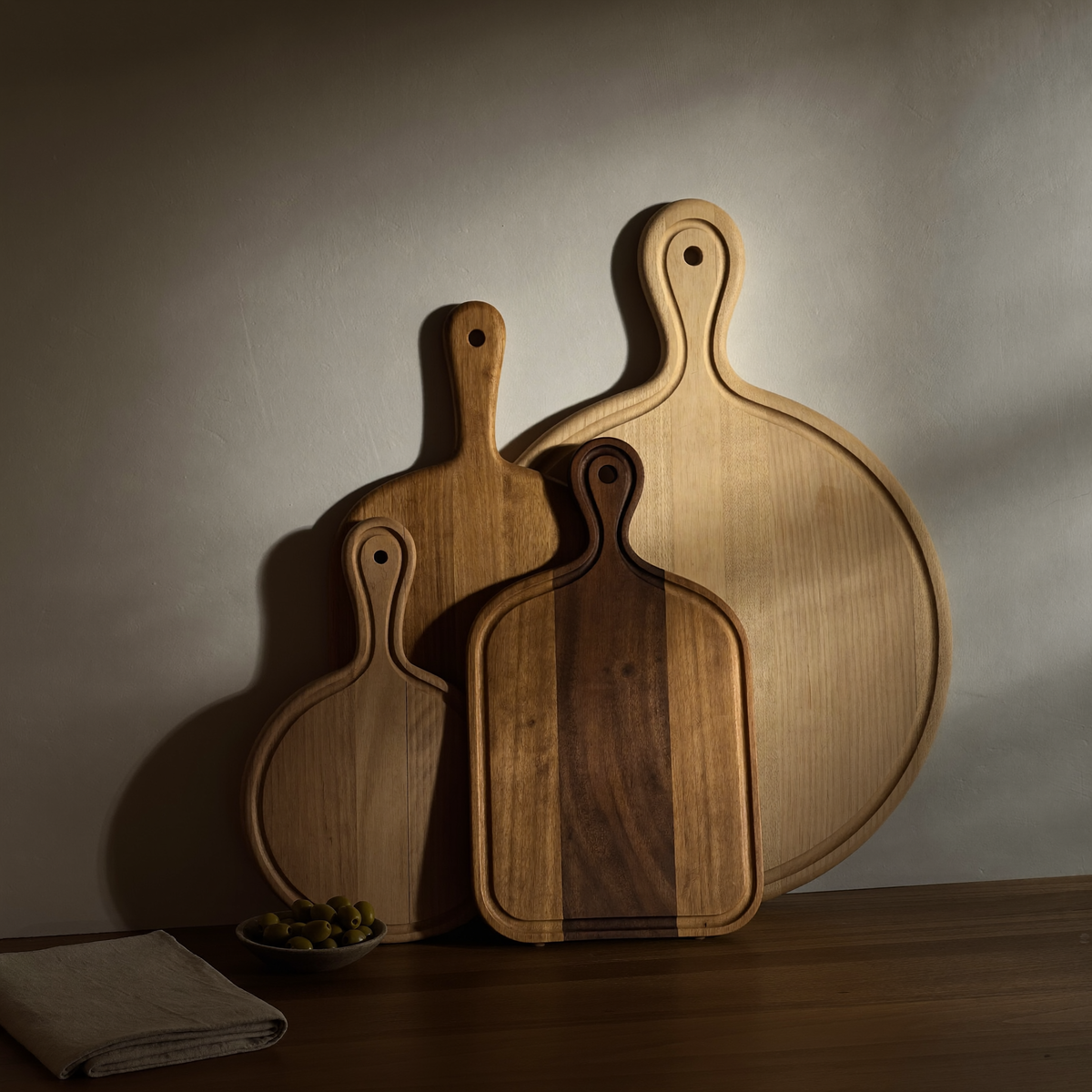 Trois planches à découper en bois d'essences différentes, avec poignée, appuyées contre un mur clair Image