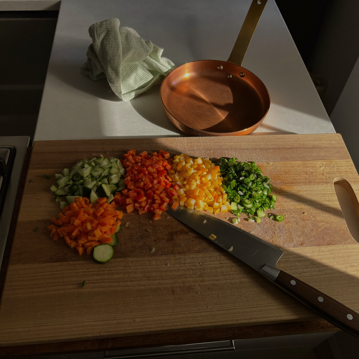 Planche à découper en bois couverte de légumes coupés en tas séparés, couteau posé dessus, casserole en cuivre derrière Image