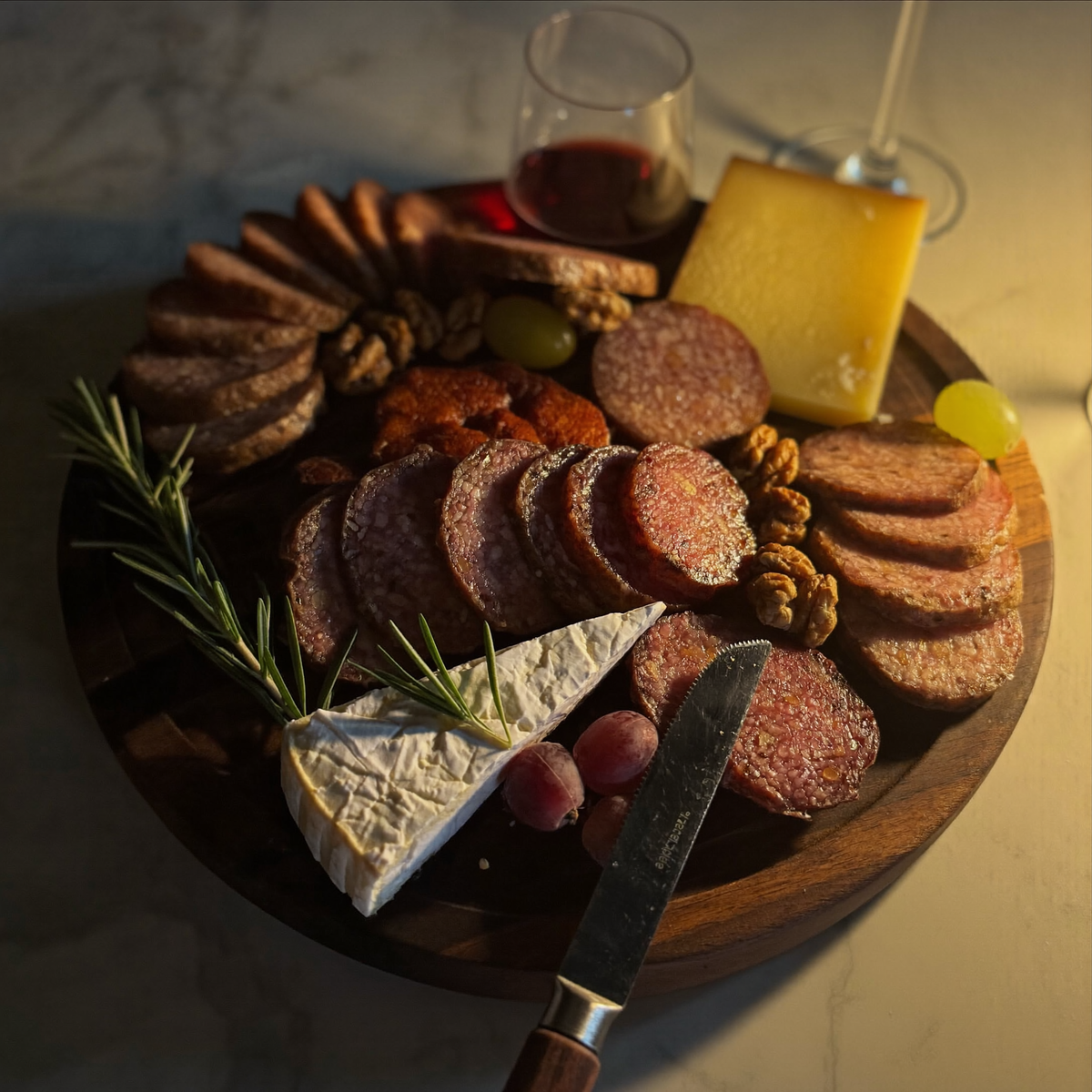 Planche de service ronde en bois garnie de saucisson tranché, de fromages, de raisin et de noix