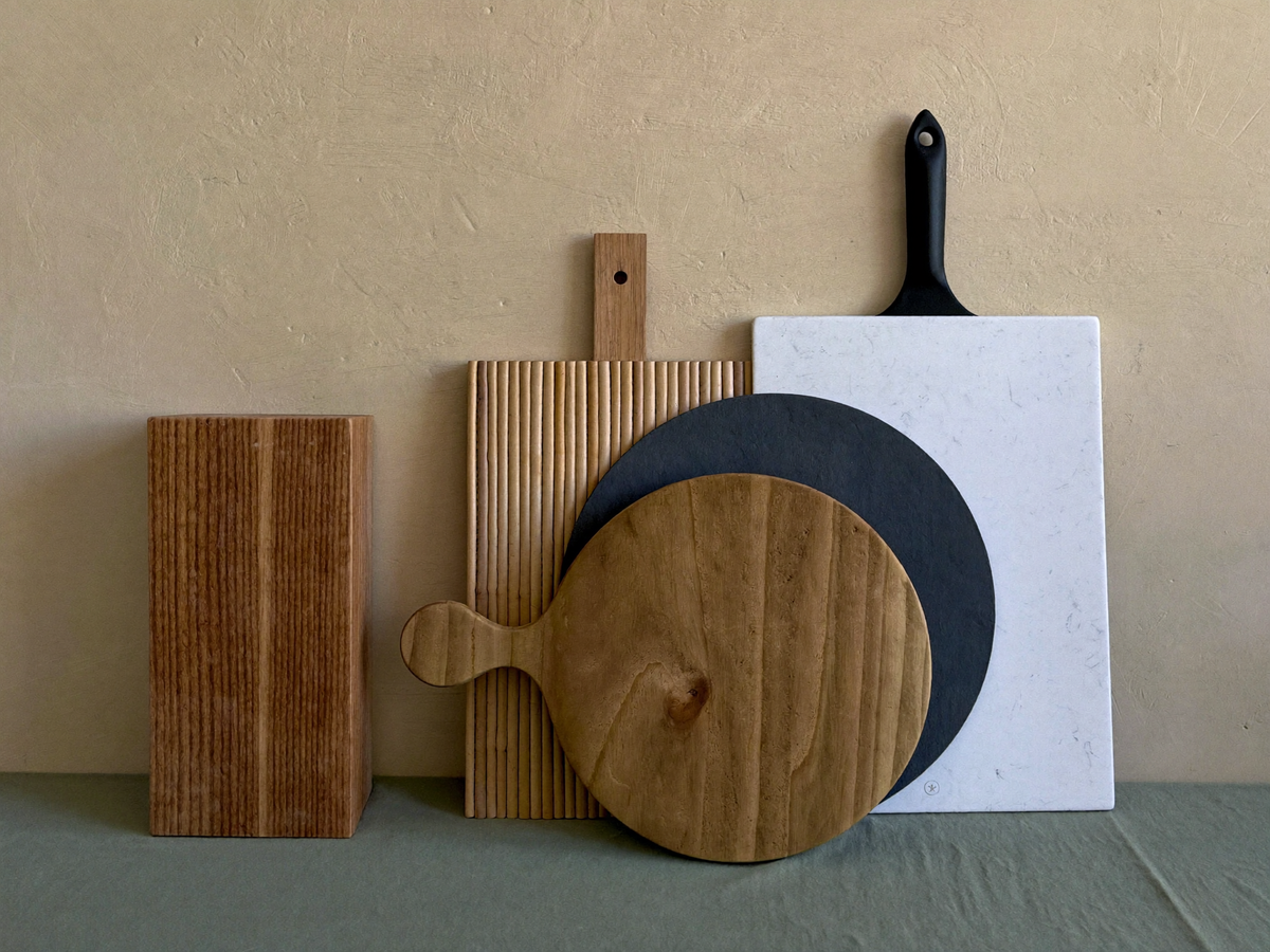 Assortiment de planches à découper de matières différentes, bois épais, bambou, planche ronde à manche et plateau sombre, appuyées contre un mur Image